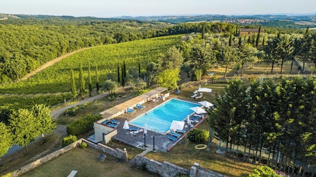 An aerial view of a villa with a swimming pool, surrounded by lush greenery and a hilly landscape.