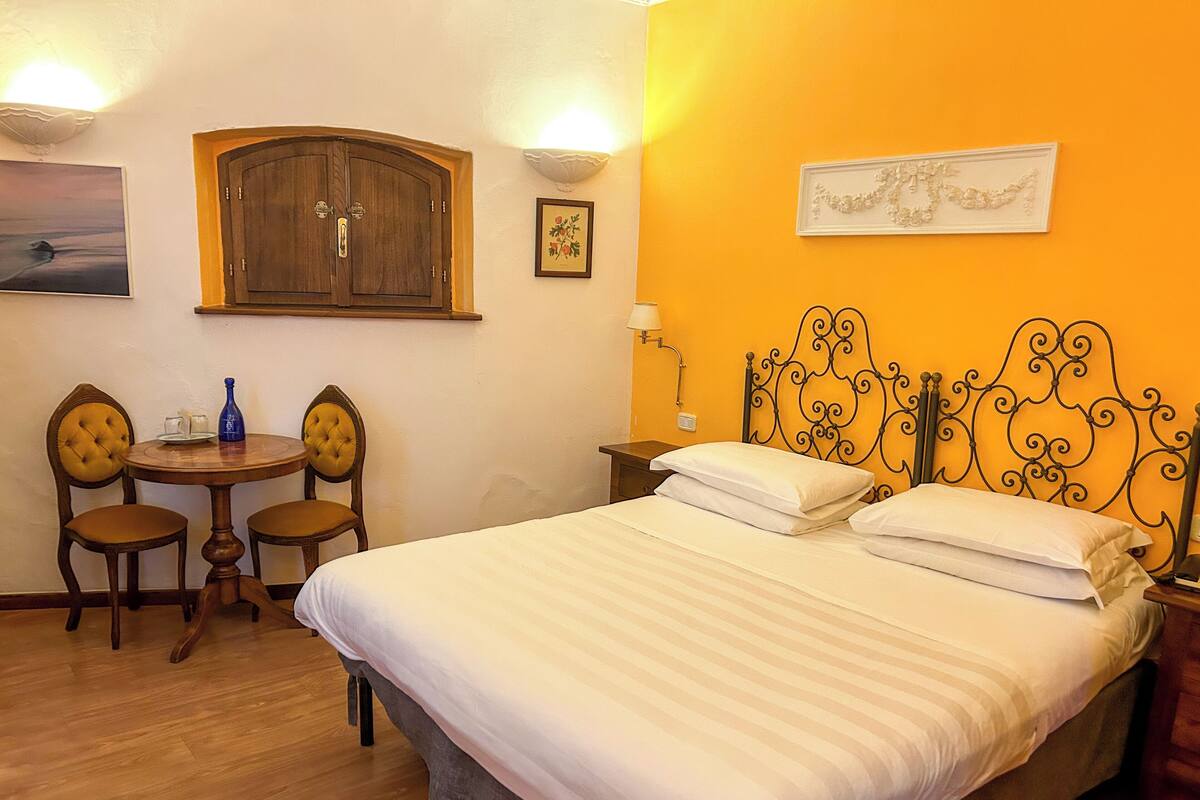 A hotel room with a bed, two chairs, a small table, and a wall-mounted lamp.