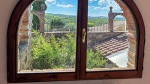 A view through a wooden-framed window with a stone archway, a brick wall, and a tiled roof.