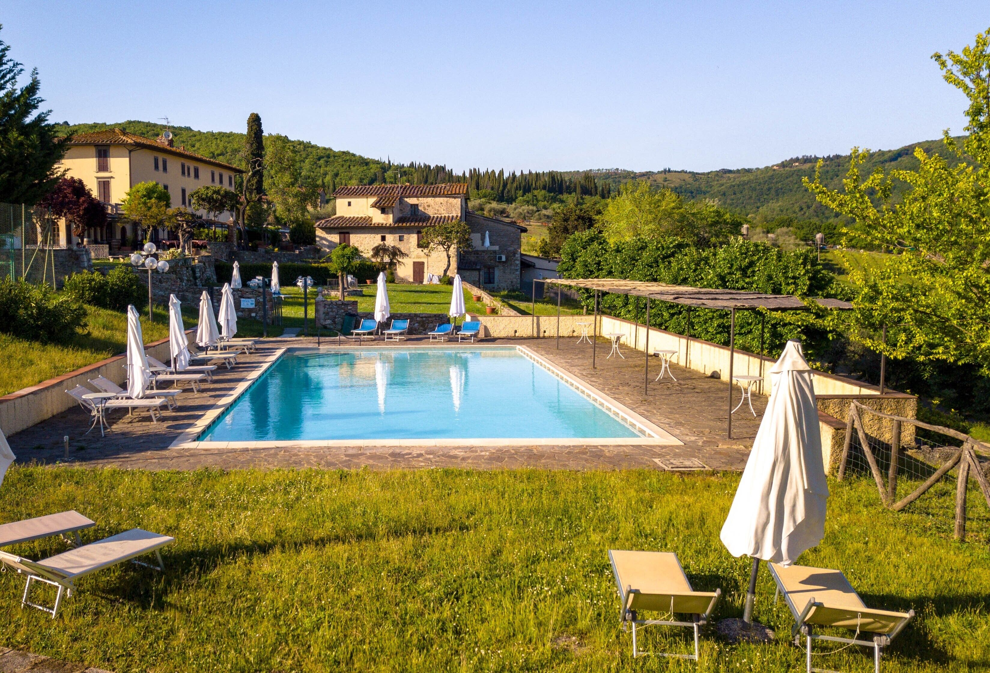 A swimming pool with lounge chairs and umbrellas, surrounded by greenery and buildings.