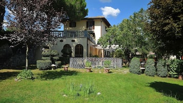 A two-story building with a balcony, surrounded by a well-maintained garden with various plants and a paved pathway.