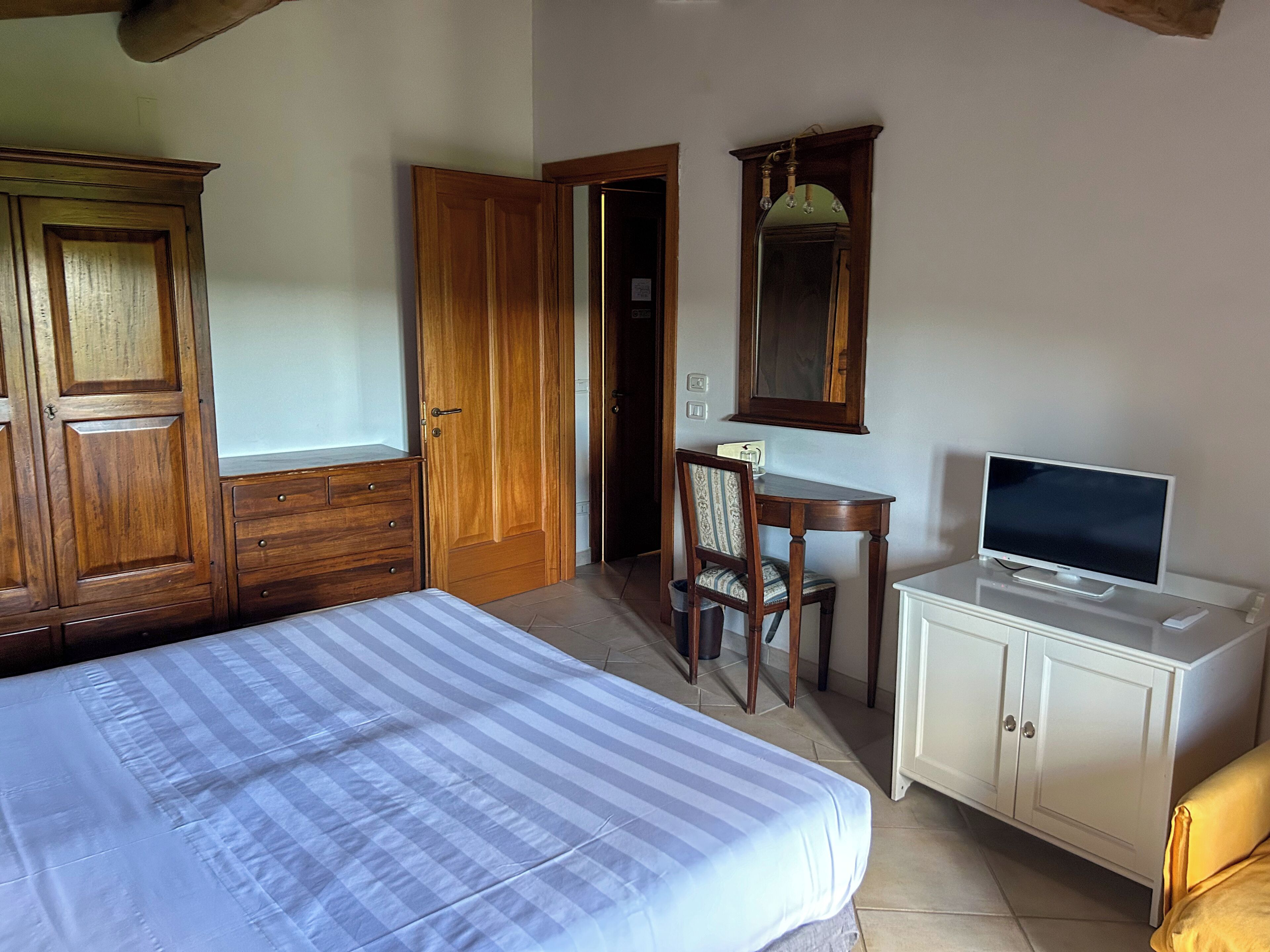 A bedroom with a bed, a desk with a computer, a chair, a television, and wooden wardrobes.