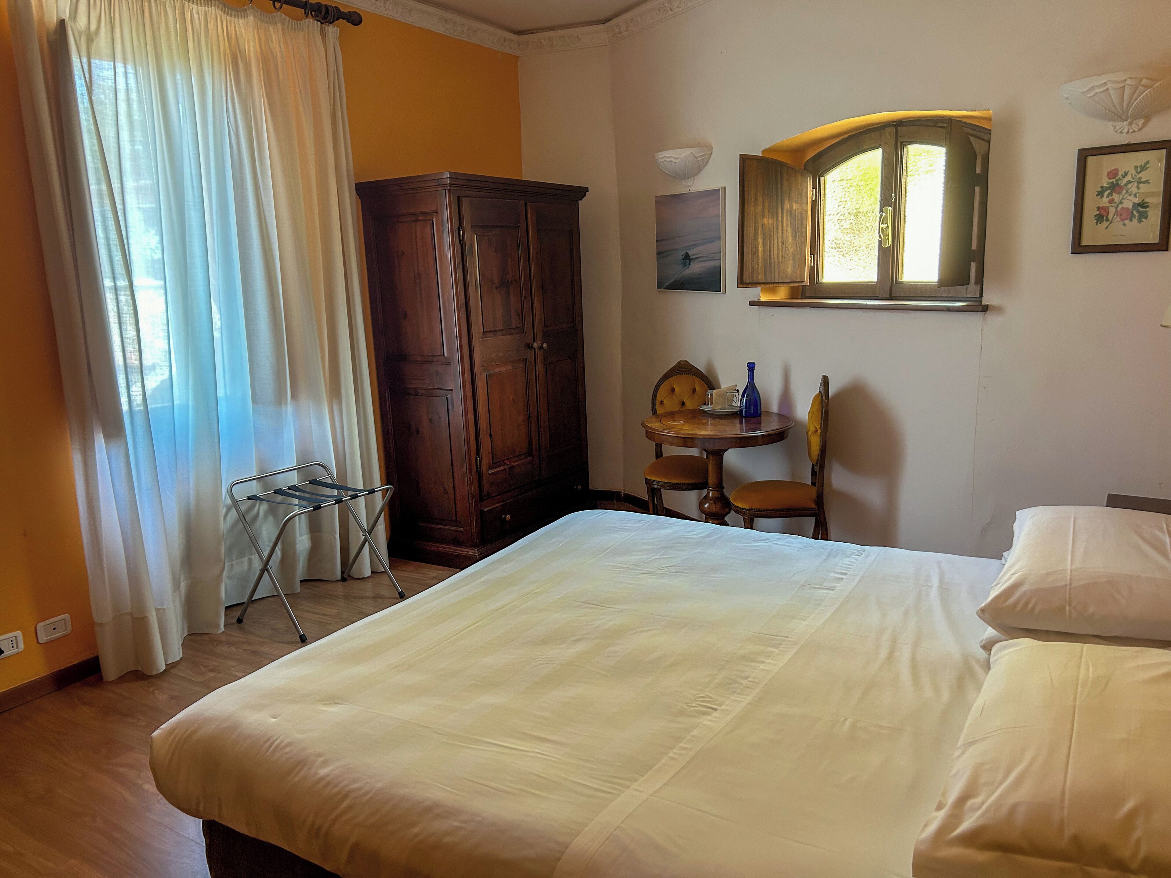 A bedroom with a bed, a wardrobe, a table with chairs, a window, and a wall-mounted lamp.