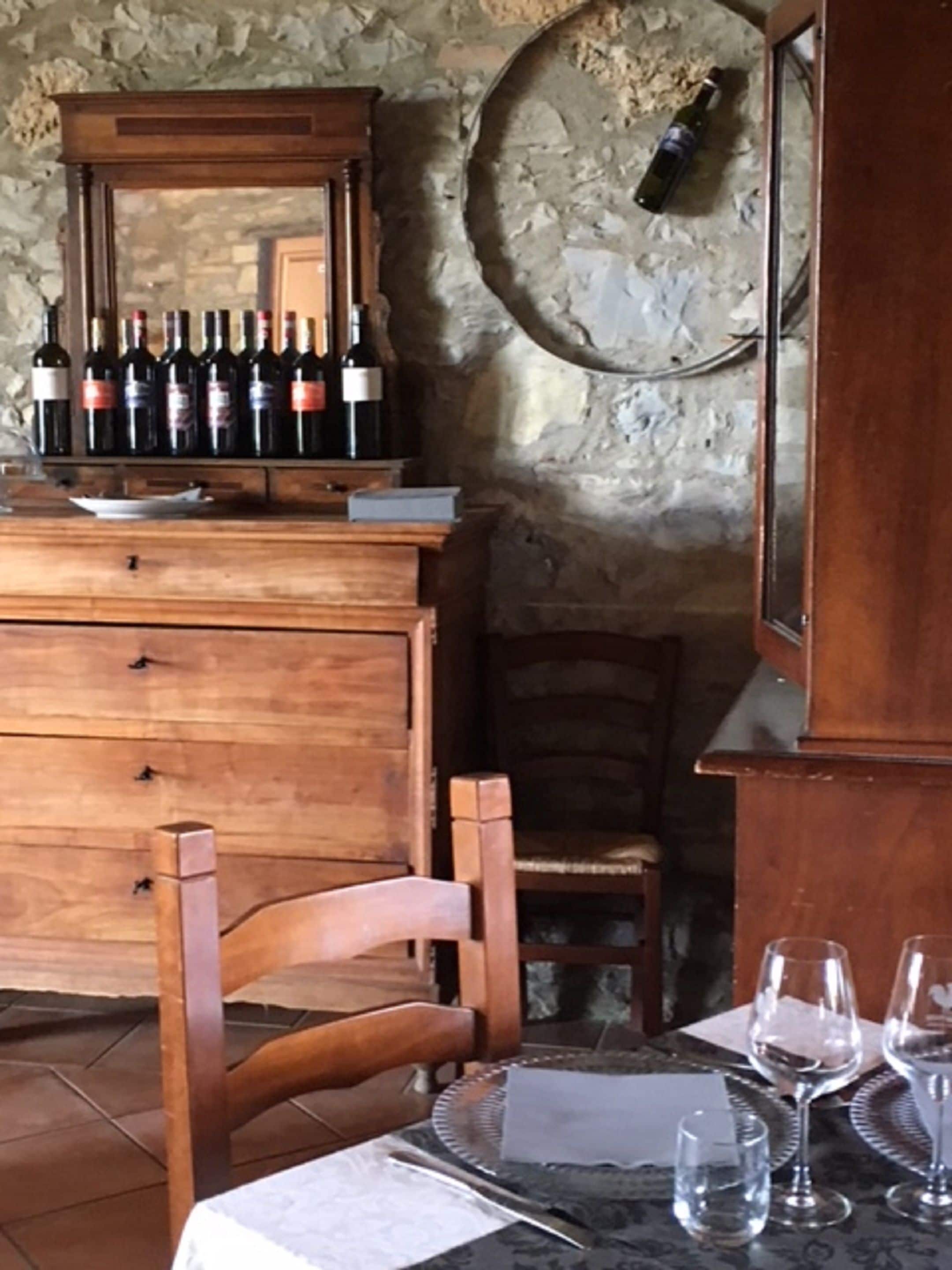 Una zona de menjador amb una taula de fusta preparada per a dues persones, una botiga de vi amb ampolles i una paret de pedra.