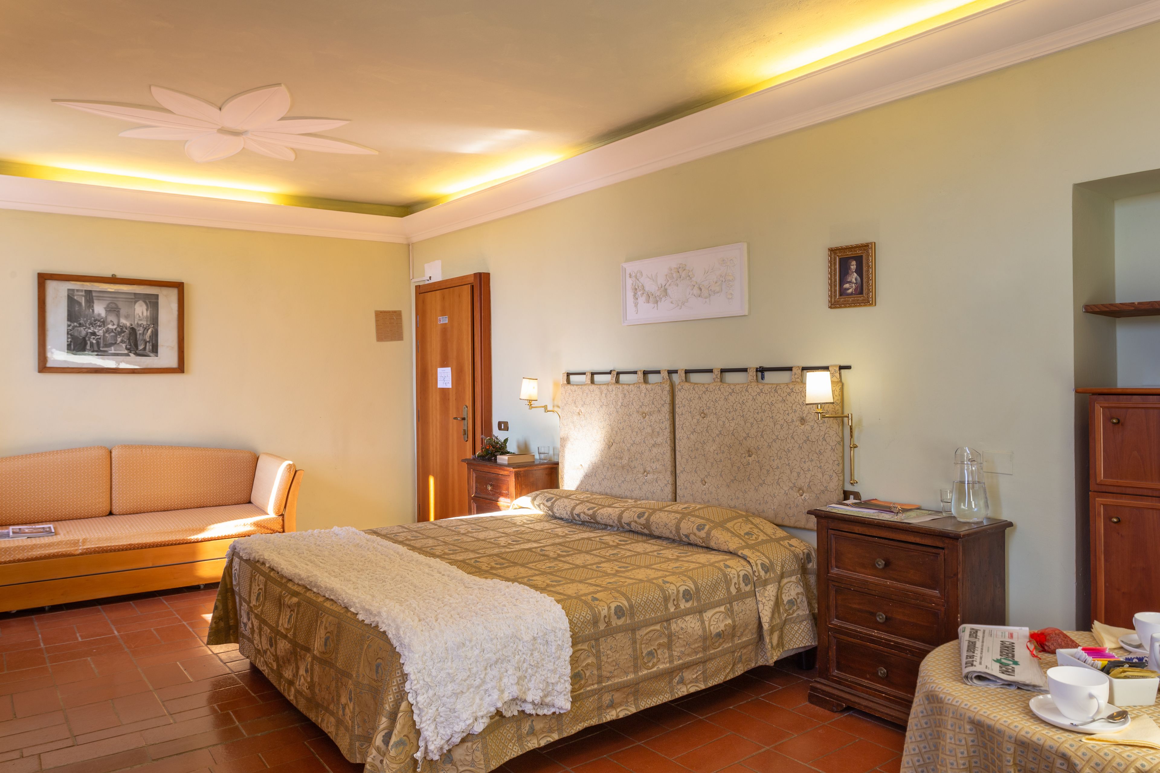 Une chambre à coucher comprenant un lit, une commode en bois, une table de chevet, une lampe, un tableau encadré et un canapé.