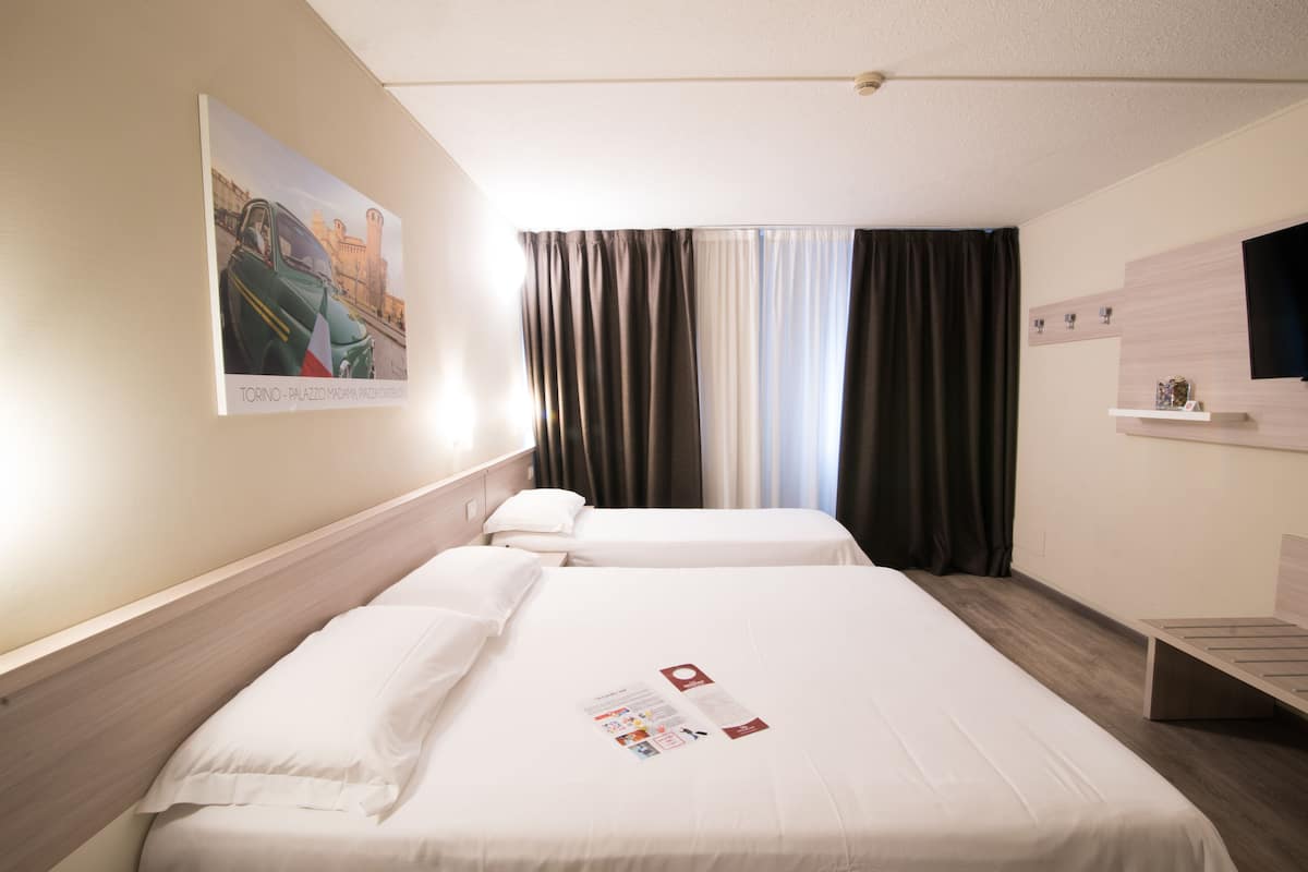 A hotel room with two beds, a large window with curtains, a wall-mounted TV, and a poster on the wall.