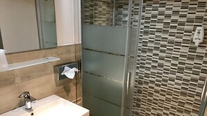 Ein Badezimmer mit Duschkabine aus Glas, einem weißen Waschbecken und einem Handtuchspender.