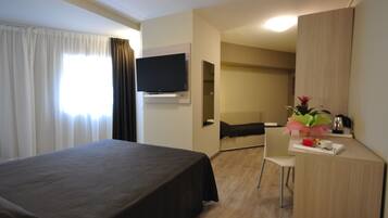Ein Hotelzimmer mit Bett, Schreibtisch mit Stuhl, flachbildfernseher an der Wand und einem Tisch mit Blumenarrangement.