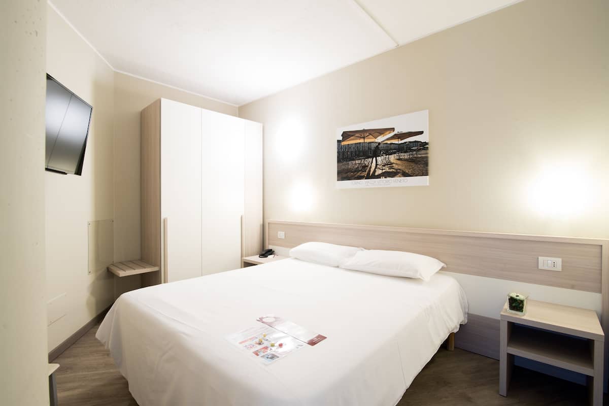 A hotel room with a bed, a nightstand, a bedside table, a wardrobe, and a wall-mounted TV.