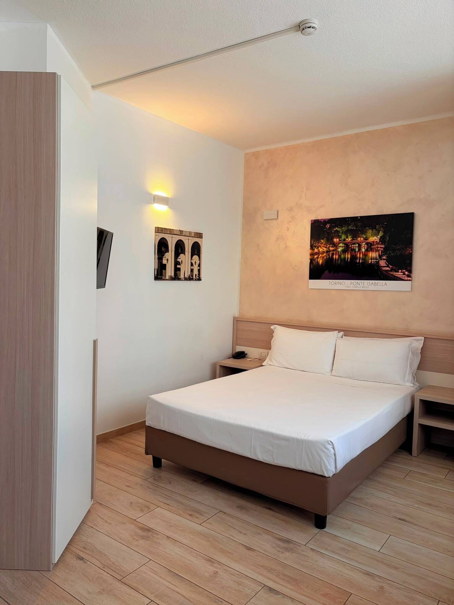 Un dormitorio con una cama, mesitas de noche, una lámpara de pared y un cuadro enmarcado.