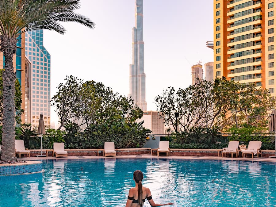 A swimming pool with lounge chairs, palm trees, and a view of the Burj Khalifa.