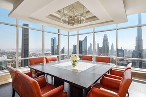 A modern conference room with a large table and red leather chairs, large windows offering a city skyline view.