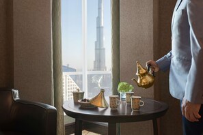 A table with a teapot, cups, and a vase, with a view of a tall building through a window.