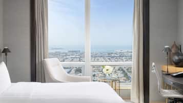 A hotel room with a large window, a bed, a chair, a desk, and a vase with flowers.
