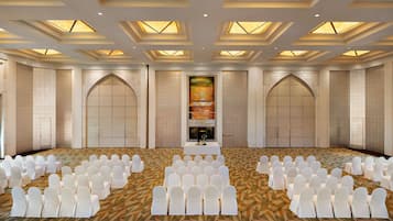 A large conference room with rows of white chairs, a central stage, and a patterned carpet.