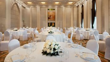 A banquet hall with round tables, white tablecloths, and floral centerpieces.