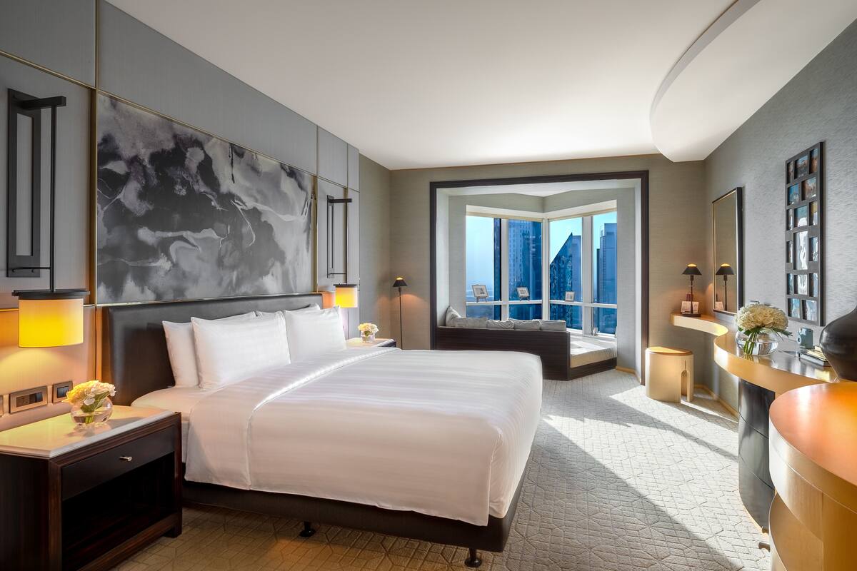 A modern hotel room with a large bed, a view of the city, and a seating area by the window.