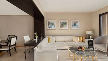 A modern living room with a sectional sofa, a dining table, and a coffee table. There are framed artworks on the wall and a lamp on a side table.