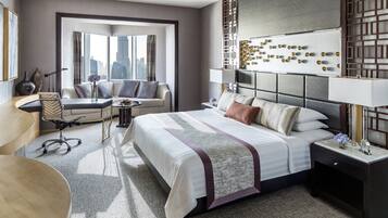 A modern hotel room with a large bed, a sofa, a desk, and a view of the city.