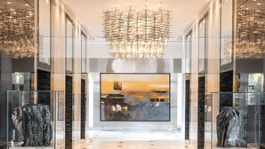 Un hall d’entrée spacieux, agrémenté d’un lustre moderne, d’un sol en marbre et de vitrines en verre où sont exposées des sculptures.