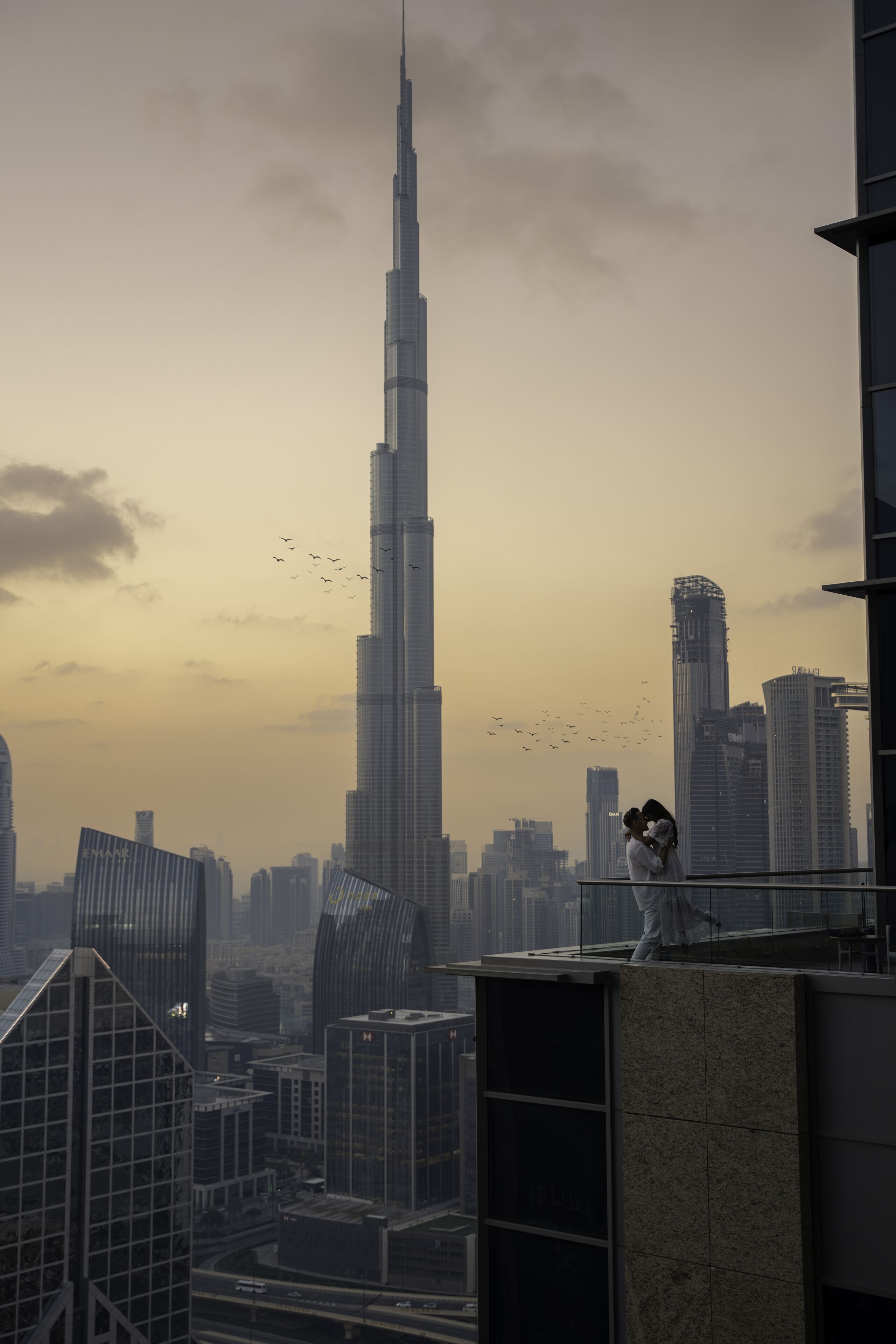 A cityscape with a prominent skyscraper, modern buildings, and a couple on a balcony.