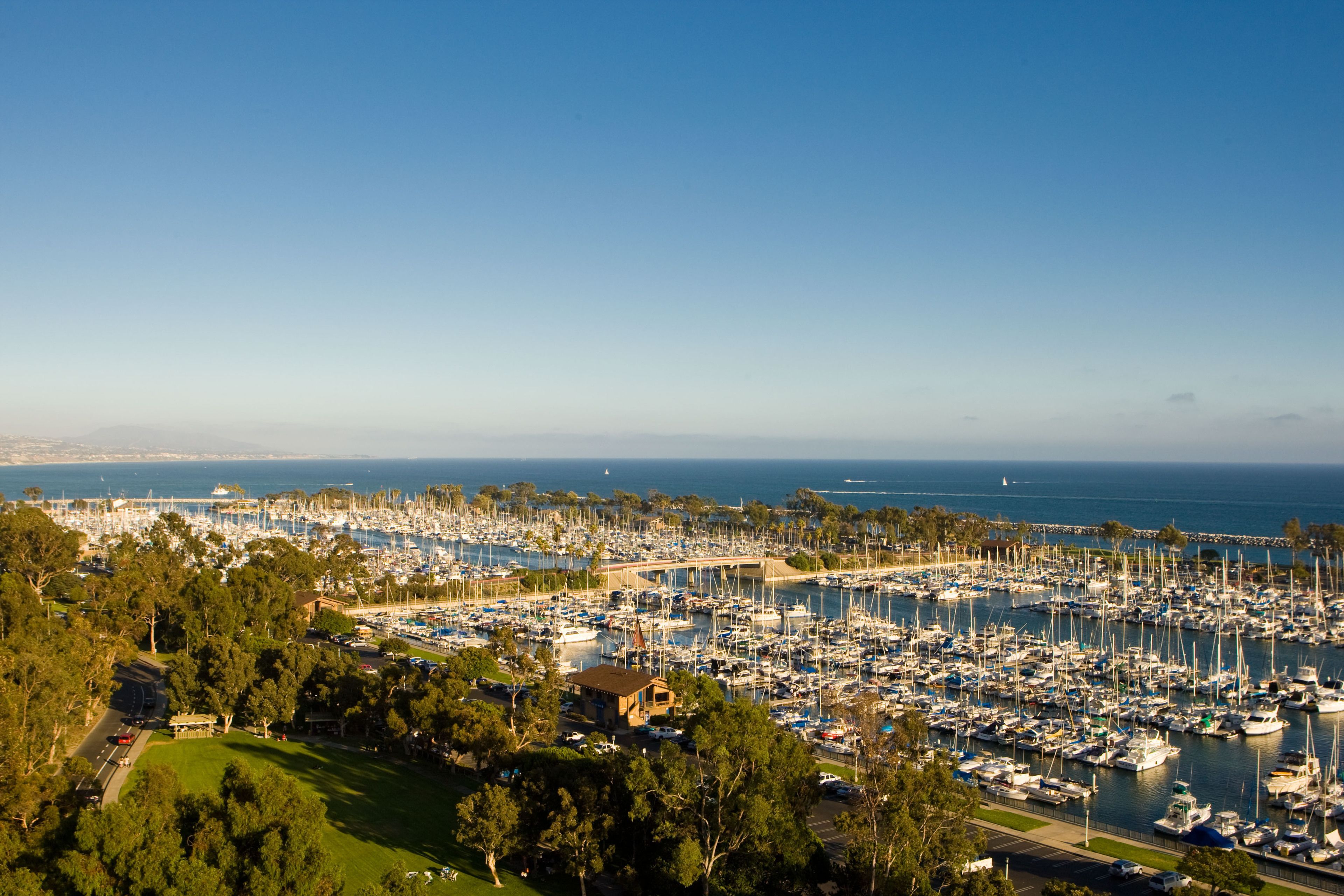 A marina with numerous boats docked, surrounded by greenery and a clear sky.