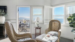 A sunlit room with wicker chairs, a small table with a tray of food and drinks, and a view of the ocean through large windows.