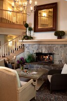 Una sala de estar acogedora con chimenea de piedra, muebles de mimbre, una mesa de centro de vidrio y una escalera con candelabro.