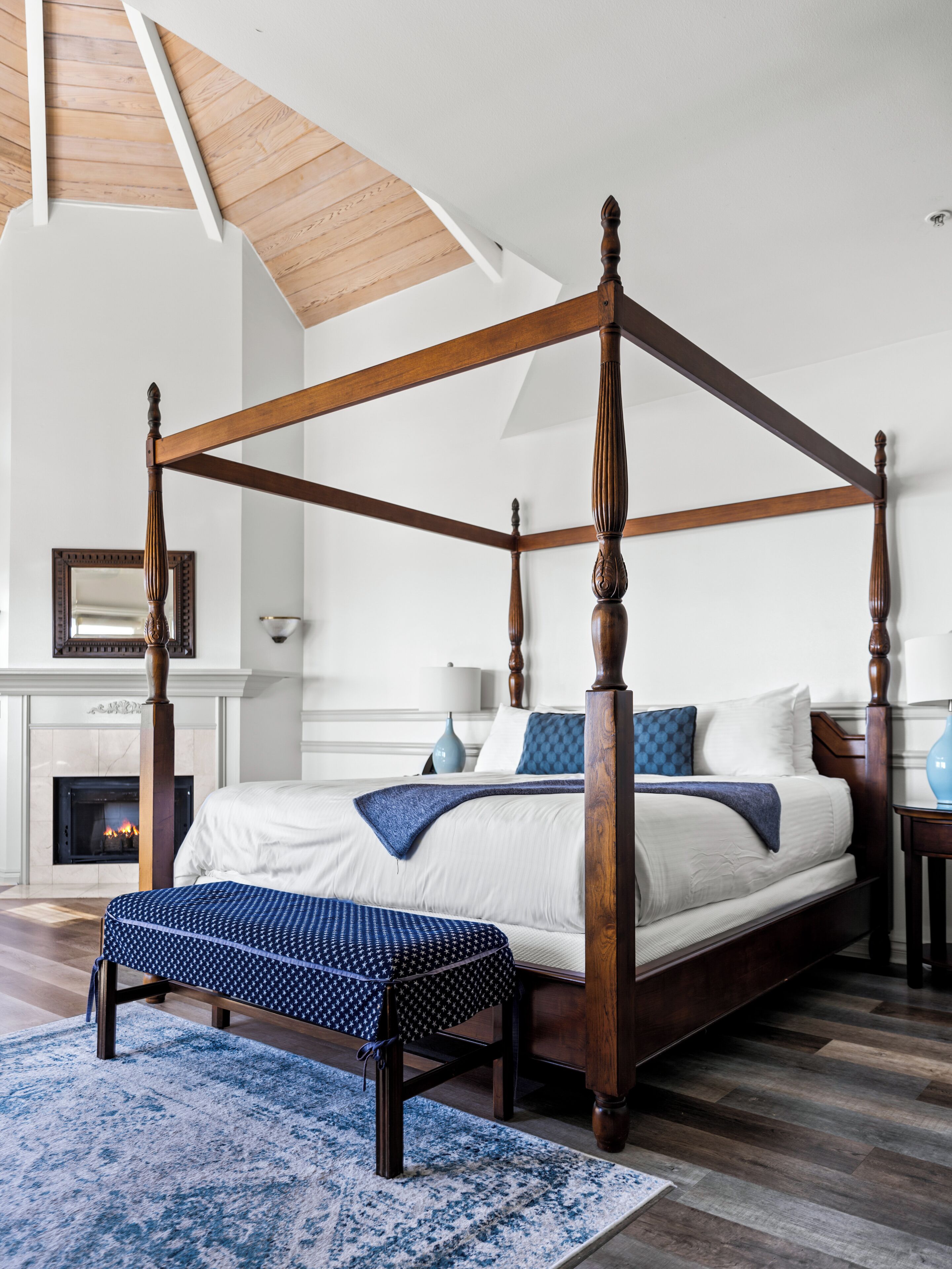 Una cama con dosel de madera, un banco de estampado azul y una alfombra azul y blanca.