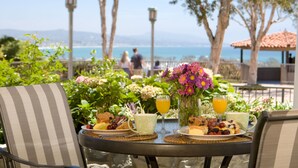 A table set for breakfast with a view of the sea, including plates of food, drinks, and a vase of flowers. - Blue Lantern Inn, A Four Sisters Inn (Dana Point)