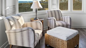 A room with striped armchairs, a sofa, and a wicker ottoman. Large windows offer a view of the outdoors. - Blue Lantern Inn, A Four Sisters Inn (Dana Point)