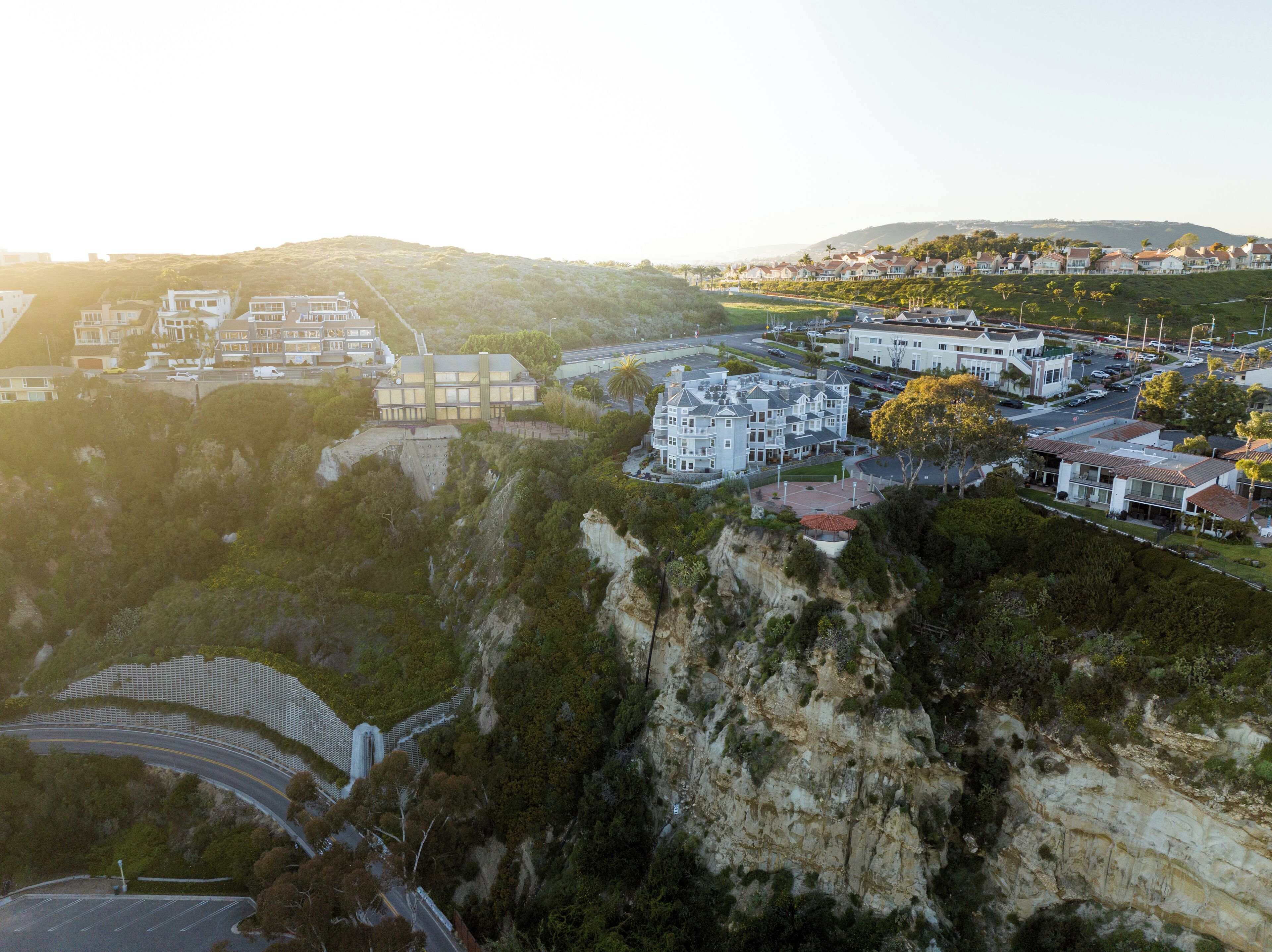A coastal town with a mix of modern and traditional architecture, including a prominent white building with a balcony and a curved road winding through the area.