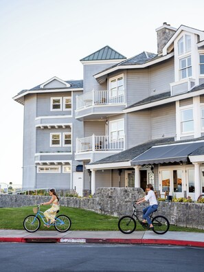 A multi-story residential building with balconies, a stone wall, and a paved driveway.