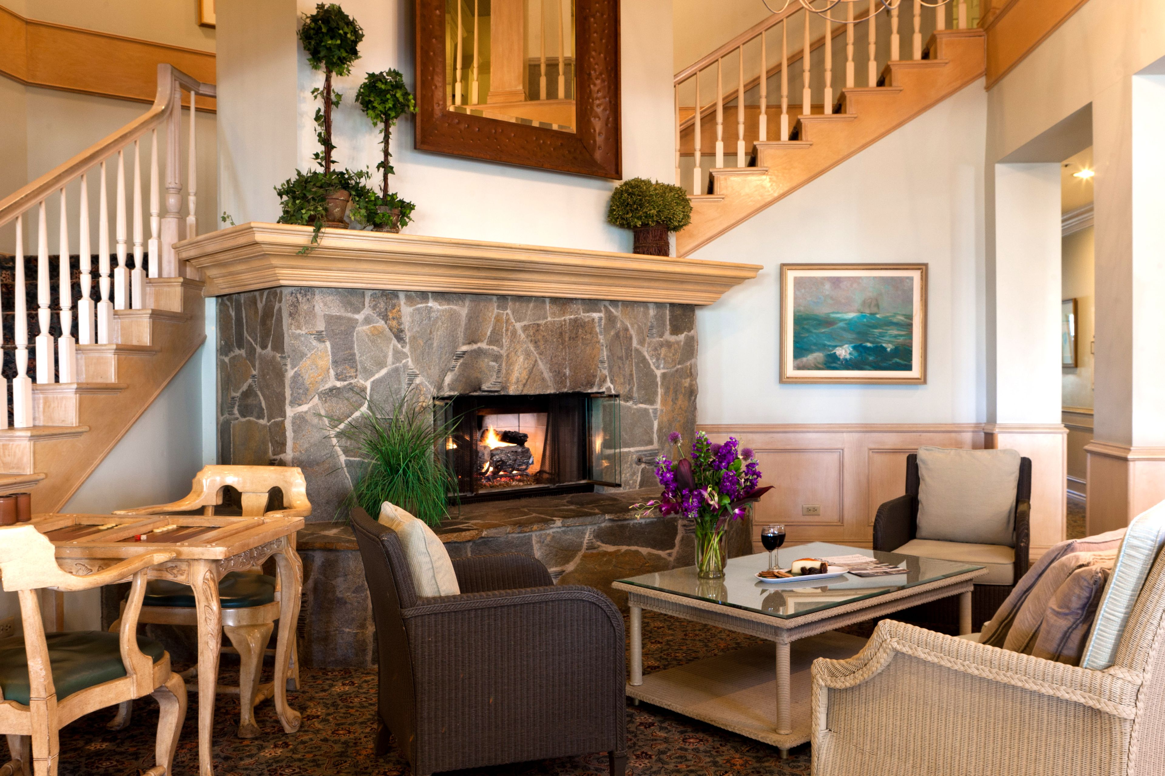 A spacious living area with a stone fireplace, comfortable seating, a staircase, and a painting on the wall.