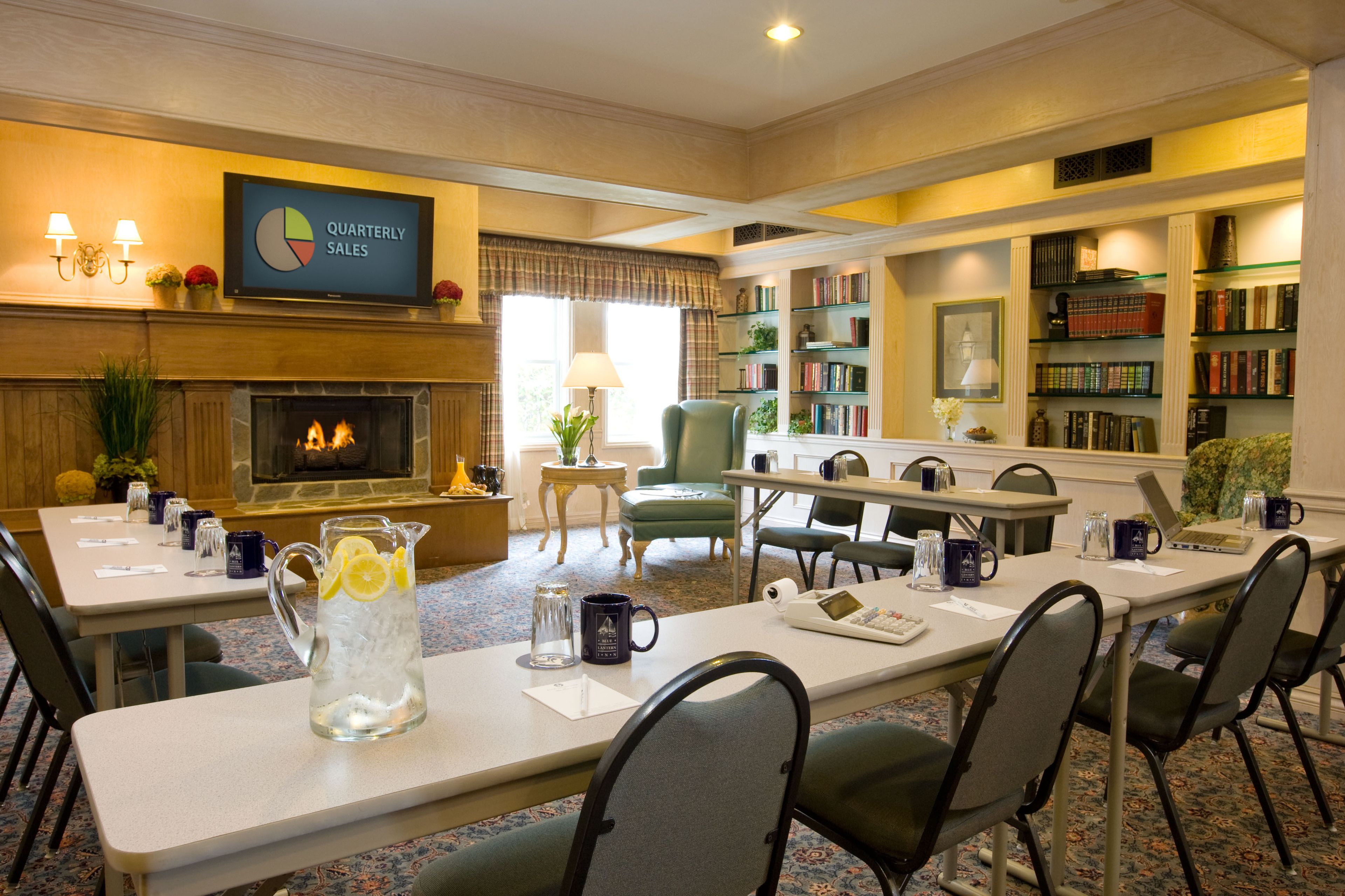 A conference room with a fireplace, a television displaying quarterly sales, and a bookshelf filled with books.