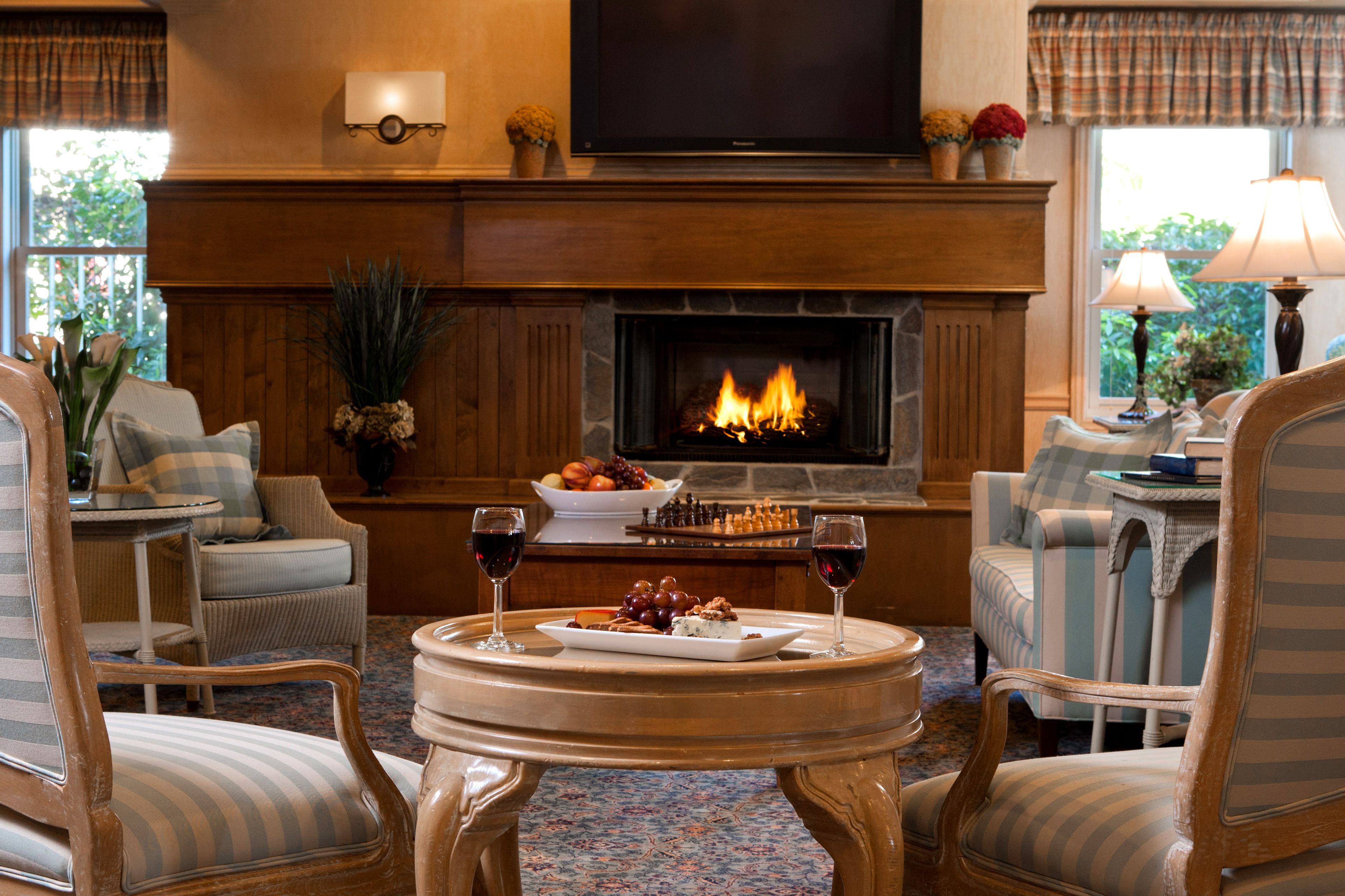 A cozy living room with a fireplace, comfortable seating, and a table with a chessboard and wine glasses.