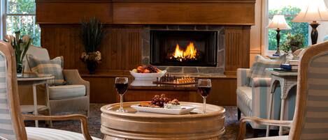 A cozy living room with a fireplace, comfortable seating, and a table with a chessboard and wine glasses.