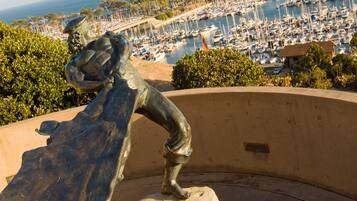A sculpture of a figure on a curved bench overlooking a marina with boats and a clear view of the ocean.