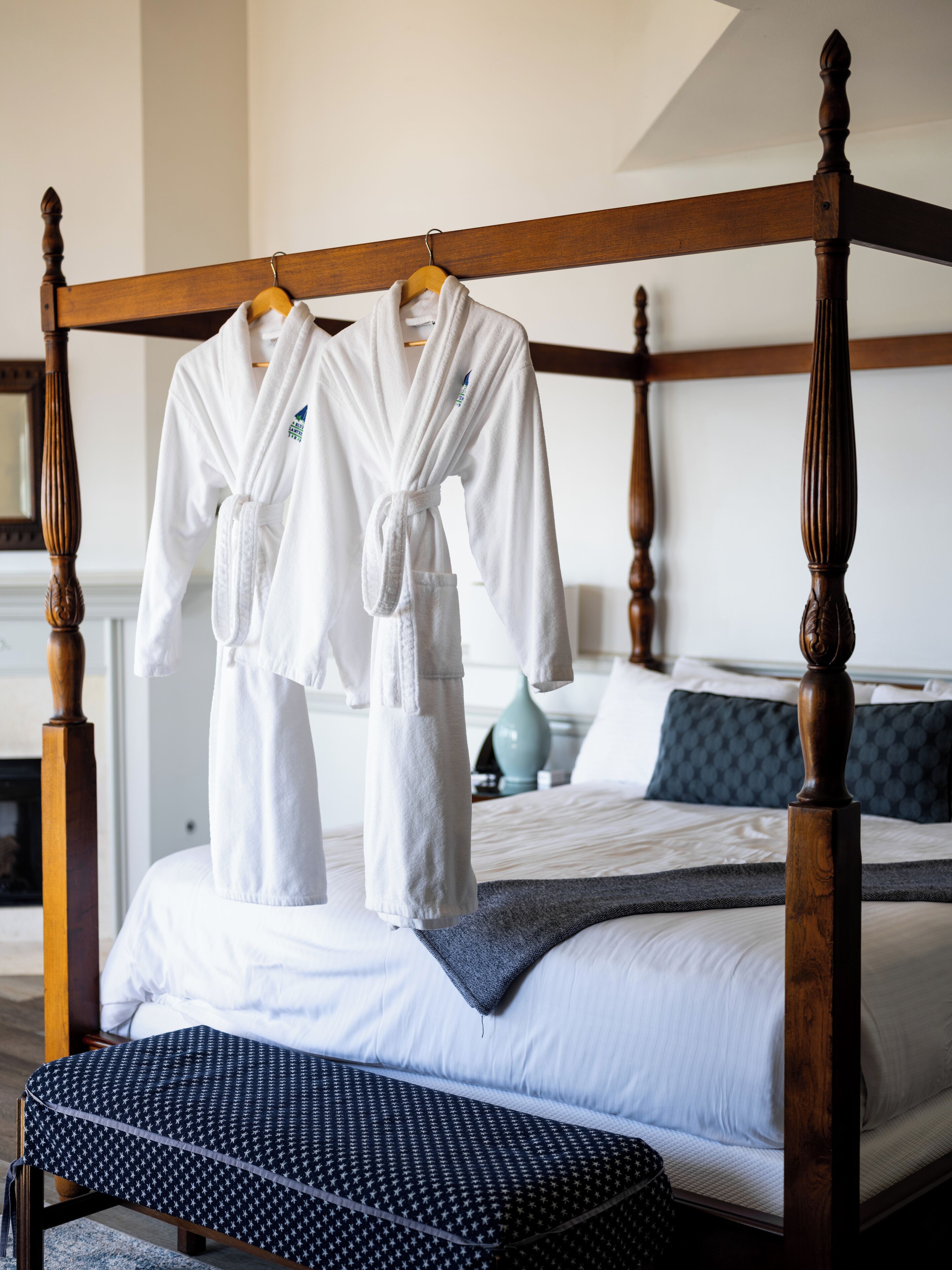 A four-poster bed with white bedding and a dark patterned throw.