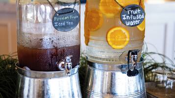 Dos dispensadores de bebidas, uno etiquetado como 'Passion Fruit Iced Tea' y el otro 'Fruit Infused Water', sobre una encimera de mármol con un plato blanco y un cuenco pequeño cerca.