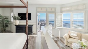 A bedroom with a large bed, a wooden four-poster bed, a TV mounted on the wall, and a view of the ocean through the windows. - Blue Lantern Inn, A Four Sisters Inn (Dana Point)