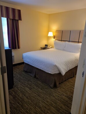 A hotel room with a large bed, a bedside table with a lamp, and a window with curtains. - Candlewood Suites Tyler by IHG (Tyler)