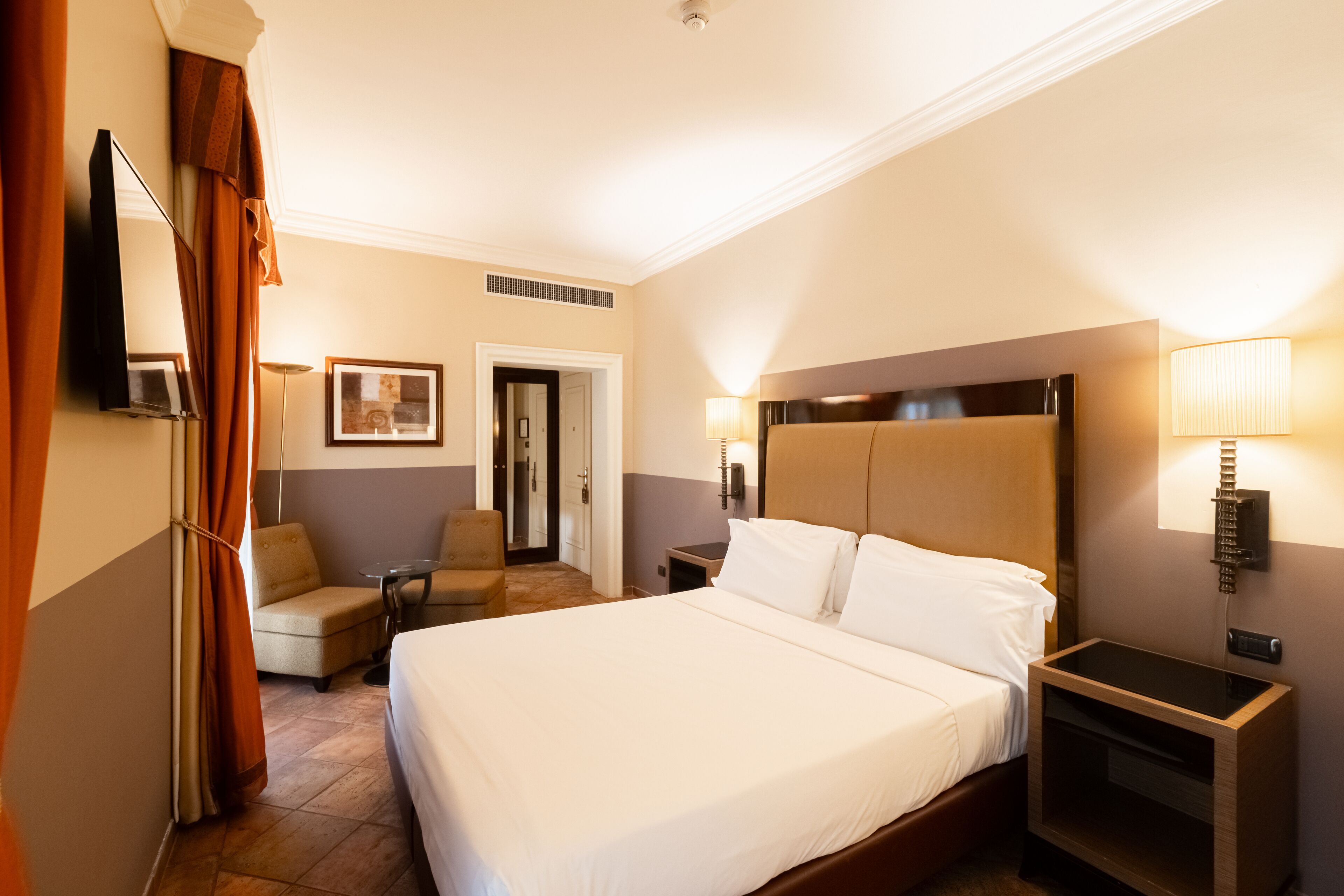 A hotel room with a large bed, a chair, a desk, a TV, and a lamp.