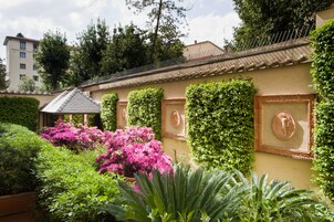 Un edificio con tetto in tegole, circondato da vegetazione rigogliosa e piante fiorite.