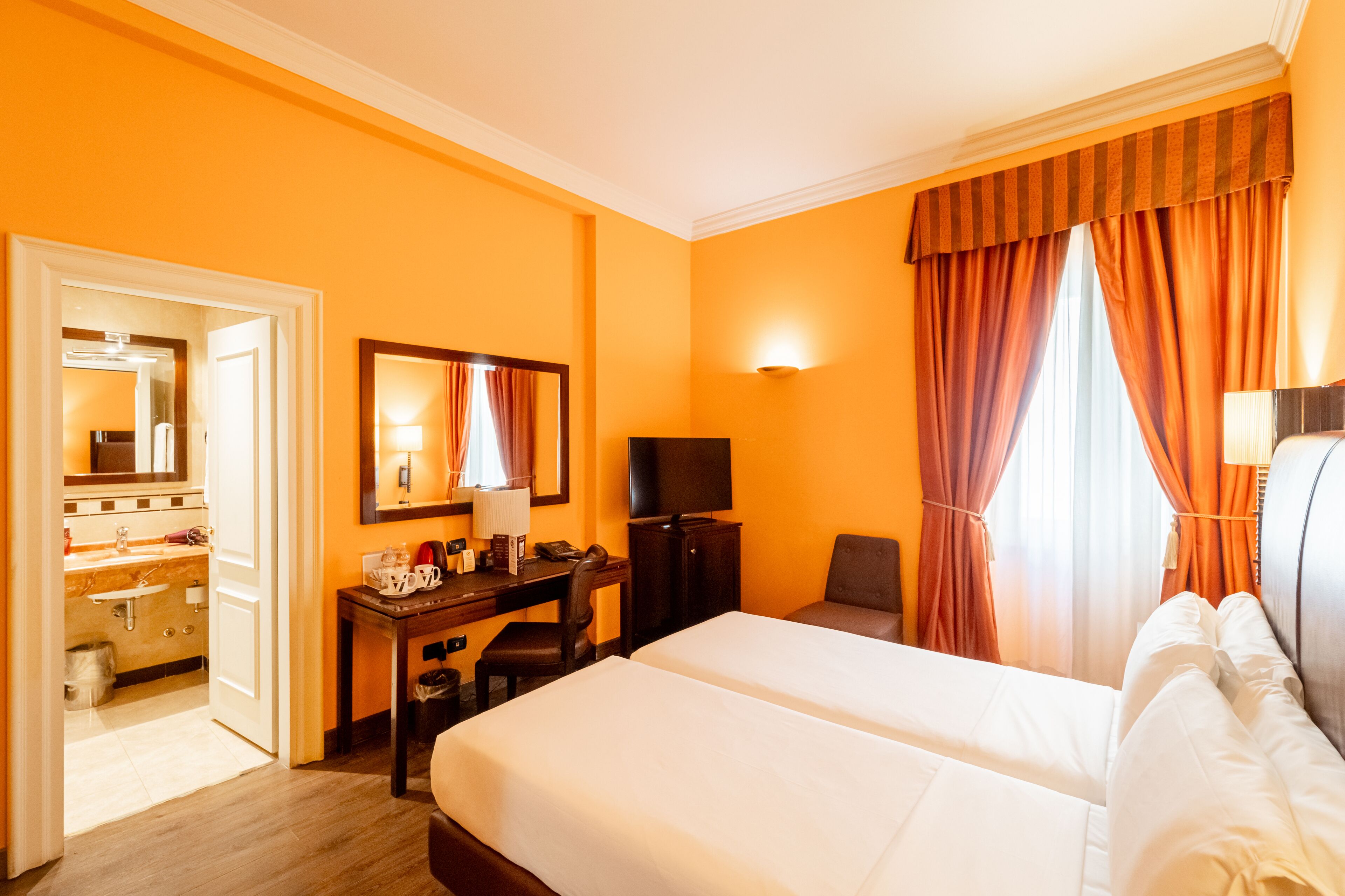 A hotel room with a large bed, a desk with a chair, a television, and a bathroom visible through an open door.