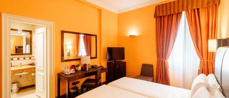 A hotel room with a large bed, a desk with a chair, a television, and a bathroom visible through an open door.