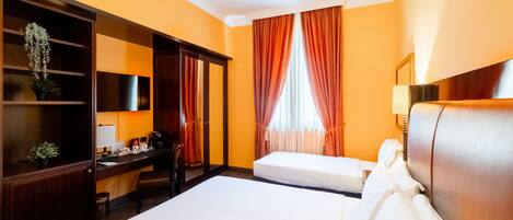 A hotel room with two beds, a desk, a chair, a wardrobe, and a window with curtains.