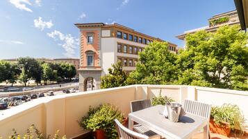 A balcony with a table and chairs, potted plants, and a view of a building with a red facade.