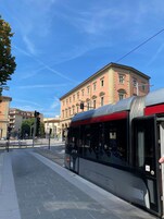 Un tram presso una stazione, cielo sereno e un edificio sullo sfondo.