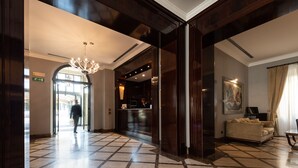 Un vestíbulo de hotel con mostrador de recepción, lámpara de araña y un sofá.
